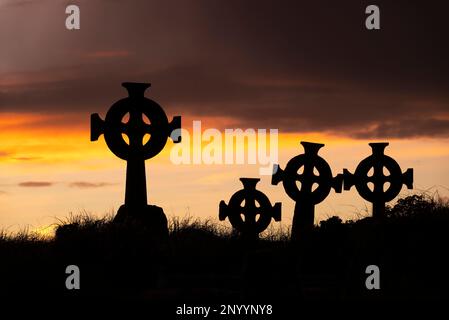 Silhouetten von Grabsteinen mit keltischen Kreuzen auf dem Cross Abbey Friedhof in der Abenddämmerung, Mullet Peninsula, County Mayo, Irland Stockfoto