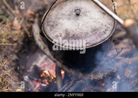 Draufsicht auf einen Gusseisentopf mit einem Deckel, der über einem brennenden Lagerfeuer hängt Stockfoto