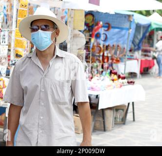 Lateinamerikanischer älterer Erwachsener mit Gesichtsschutzmasken und Hut beim Gehen in plaza, neuer normaler Covid-19 Stockfoto