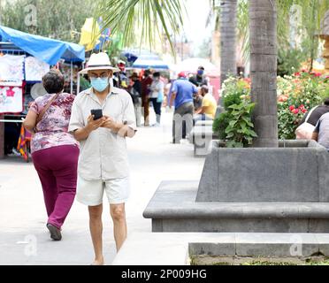 Lateinamerikanischer älterer Erwachsener mit Gesichtsschutzmasken und Hut beim Gehen in plaza, neuer normaler Covid-19 Stockfoto