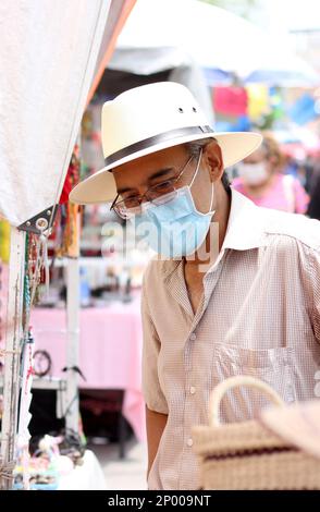 Lateinamerikanischer älterer Erwachsener mit Gesichtsschutzmasken und Hut beim Gehen in plaza, neuer normaler Covid-19 Stockfoto
