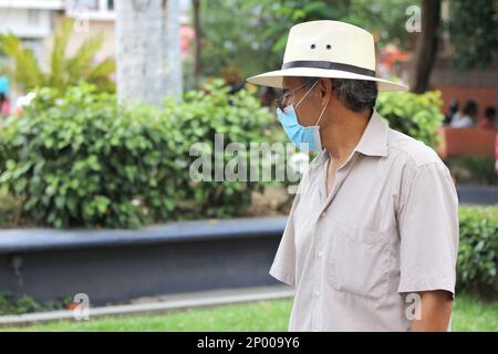 Lateinamerikanischer älterer Erwachsener mit Gesichtsschutzmasken und Hut beim Gehen in plaza, neuer normaler Covid-19 Stockfoto