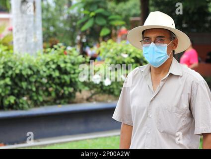 Lateinamerikanischer älterer Erwachsener mit Gesichtsschutzmasken und Hut beim Gehen in plaza, neuer normaler Covid-19 Stockfoto