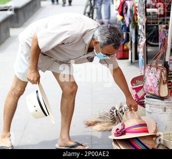 Lateinamerikanischer älterer Erwachsener mit Gesichtsschutzmasken und Hut beim Gehen in plaza, neuer normaler Covid-19 Stockfoto