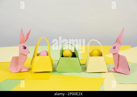 Zwei rosafarbene Osterhasen aus Papier, Origami-Kunsthandwerk und Eierkörbe, Platz für Text Stockfoto
