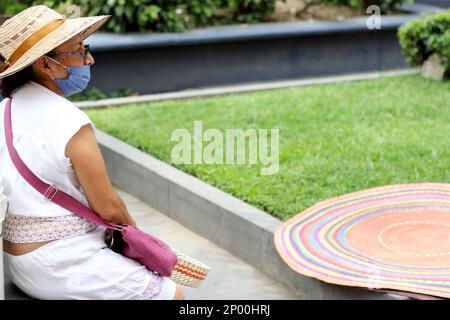 Ältere Erwachsene Frau mit Schutzmaske und Hut im öffentlichen Garten mit Hut, neuer normaler Covid-19 Stockfoto