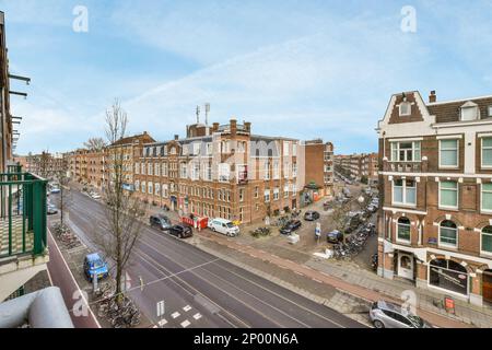 Amsterdam, Niederlande - 10. April 2021: Eine Stadtstraße mit Autos, die an der Seite geparkt sind, und Gebäuden in der Ferne, die von einem überquerten Balkon übernommen werden Stockfoto