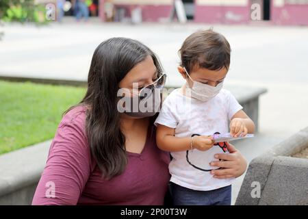 Mutter und zweijähriges latinmädchen mit Schutzmasken auf dem platz, neue normale covid-19 Stockfoto