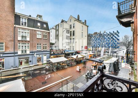 Amsterdam, Niederlande - 10. April 2021: Eine Stadt mit Gebäuden und Menschen auf der Straße im Vordergrund - Bild aus einem offenen Balkonfenster Stockfoto