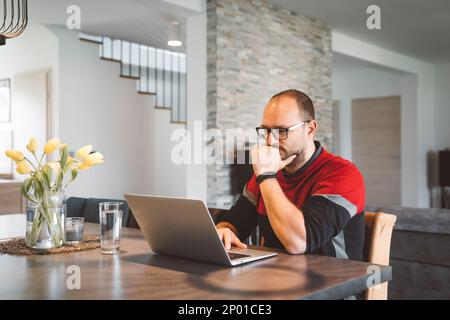 Ein erwachsener Kaukasier, der ein paar Tage die Woche von zu Hause aus arbeitet, im Wohnzimmer Stockfoto