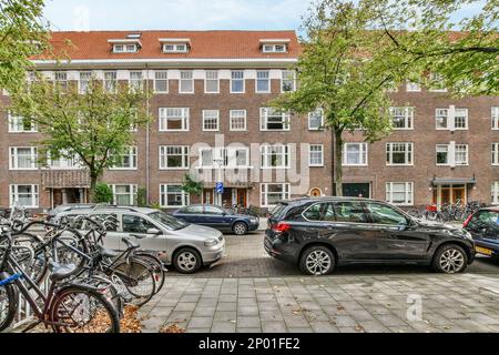 Einige Autos parkten vor einem Ziegelgebäude mit vielen Fenstern in der oberen und unteren Hälfte des Gebäudes Stockfoto