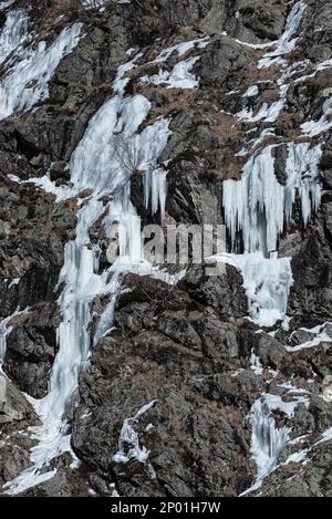 Mehrere gefrorene Wasserströme, die im Winter in Chamonix, Frankreich, Eis und Eiszapfen auf einem trockenen felsigen Berghang bilden Stockfoto