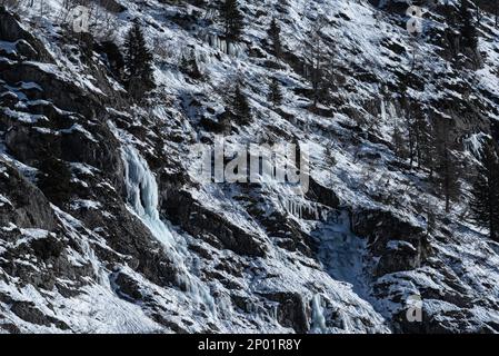 Mehrere gefrorene Wasserströme, die im Winter in Chamonix, Frankreich, Eis und Eiszapfen auf einem trockenen felsigen Berghang bilden Stockfoto