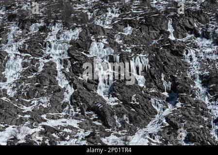 Mehrere gefrorene Wasserströme, die im Winter in Chamonix, Frankreich, Eis und Eiszapfen auf einem trockenen felsigen Berghang bilden Stockfoto