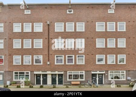 Amsterdam, Niederlande - 10. April 2021: Eine Stadtstraße mit Autos, die an der Seite geparkt sind und Menschen, die die Straße entlang laufen Stockfoto