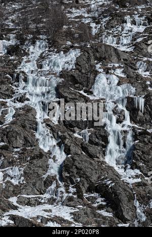 Mehrere gefrorene Wasserströme, die im Winter in Chamonix, Frankreich, Eis und Eiszapfen auf einem trockenen felsigen Berghang bilden Stockfoto