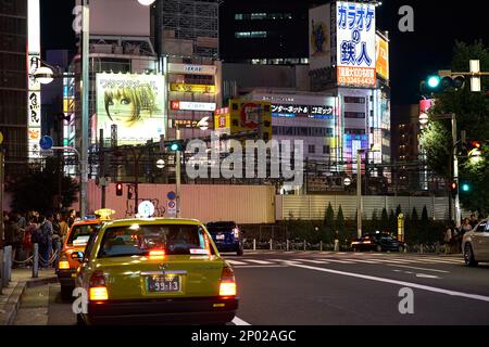 Japanische Taxis warten in der Nähe einer weißen Zebrakreuzung mit großen Neon-Werbetafeln auf den umliegenden Gebäuden in Tokio, Japan Stockfoto