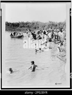 Pilger baden im Jordan, nachdem das Wasser vom Priester der griechisch-orthodoxen Kirche gesegnet wurde. Frank and Frances Carpenter Collection, Copyright by Underwood & Underwood, New York, Taufen, Jordan River, 1880-1900, Rites & Ceremonies, Jordan River, 1880-1900, Jordan River, 1880-1900. Stockfoto