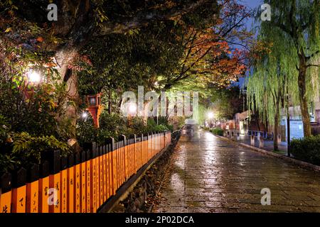 Ein wunderschöner Nachtsicht auf das nasse zinnoberfarbene orangefarbene Holztor und Kopfsteinpflaster einer Seitenstraße in Kyoto, Japan Stockfoto