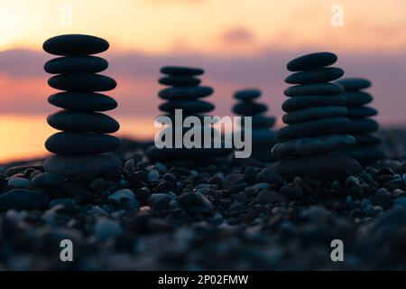 Ausgewogene Kieselpyramide am Strand bei Sonnenuntergang mit Meer im Hintergrund. Zen Steine am Strand, Meditation, Spa, Harmonie, Ruhe. Stockfoto