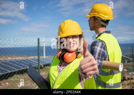Glückliche Ingenieurin zeigt Daumen nach oben auf der Solarfarm. Stockfoto