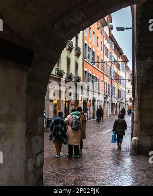 Annecy, Frankreich - 7. Januar 2022: Menschen, die bei regnerischem Winterwetter in der mittelalterlichen historischen Altstadt von french Annecy mit bunten Fassaden spazieren gehen Stockfoto