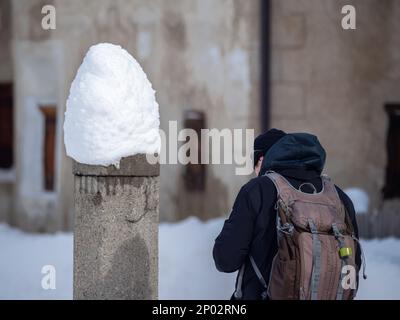 Cinuos-Chel, Schweiz - 3. Februar 2022: Ein Mann mit Rucksack in einem verschneiten Dorf Engadine, Schweiz Stockfoto