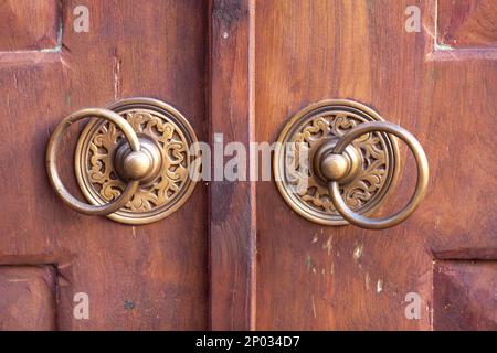 Nahaufnahme von zwei Türgriffen aus Messing an einer alten Holztür. Stockfoto