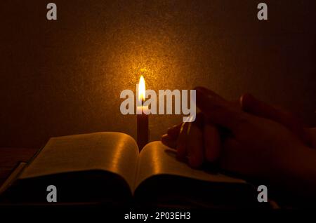 Brennende Kerze auf einem offenen Buch in einem dunklen Raum mit Kopierraum. Eine heilige bibel mit brennender Kerze lesen Stockfoto