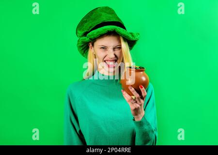 St. Patrick's Day. Irische Traditionen. Wütendes blondes Mädchen mit grünem Leprechaun-Hut und einem Topf Gold. St. Patrick Day Frau mit einem Haufen Geld. Weiblich Stockfoto