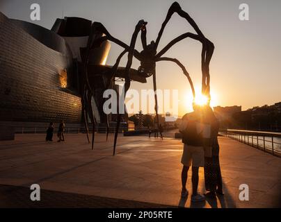 Bilbao, Spanien - 02. August 2022: Ein paar Touristen machen ein Selfie bei Sonnenuntergang neben der Spinne, der Skulptur von Louise Bourgeois mit dem Titel Mamam in Th Stockfoto