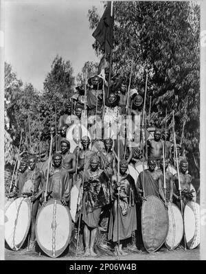 Eine Gruppe von Eingeborenen in KaEnvirondo, die sich in einer stehenden Pyramide mit Speeren und Schilden posierten. Ca. 191-, in Afrika. Frank and Frances Carpenter Collection , Veröffentlicht in: 'The World and its Cultures' Kapitel des Buches große Fotografien aus der Kongressbibliothek, 2013, Warriors,Africa,1910-1920, Shields,1910-1920, Speere,1910-1920. Stockfoto