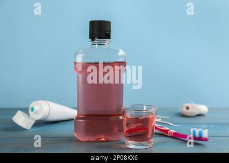 Flasche und Glas mit Mundspülung in der Nähe anderer Mundpflegeprodukte auf hellblauem Holztisch Stockfoto