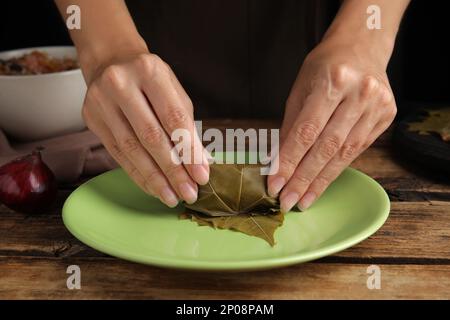 Frau, die gefüllte Traubenblätter auf einem Holztisch zubereitet, Nahaufnahme Stockfoto