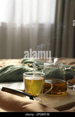 Holztablett mit frisch gebrühtem Tee auf dem Bett im Zimmer. Gemütliche Atmosphäre Stockfoto
