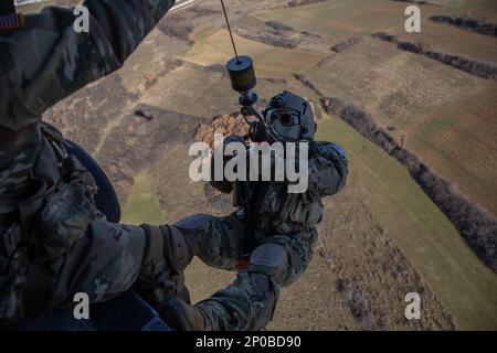 Sgt. 1. Class Anthony Bonillas, ein Soldat der Kosovo Force (KFOR) Regional Command-East (RC-E) mit der medizinischen Evakuierungseinheit, die Charlie Company zugewiesen wurde, 2. Bataillon, 149. Aviation Regiment, bereitet sich darauf vor, auf den Boden abgesenkt zu werden, während er eine Hebeoperation von einem UH-60 Black Hawk Helikopter in Camp Bondsteel durchführt, Kosovo am 6. Januar 2023. Stockfoto