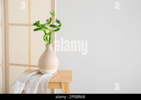 Faltsieb und Vase mit Bambuspflanze auf dem Tisch nahe der grauen Wand Stockfoto