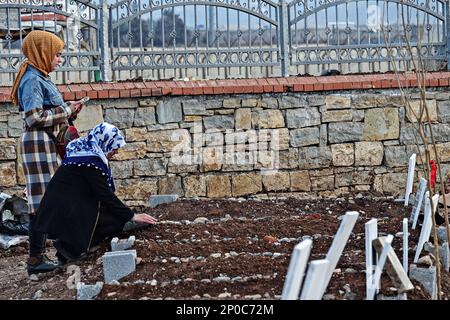 Diyarbakir, Türkei, 02/03/2023, eine junge Frau wird gesehen, wie sie den Koran für ihren Verwandten liest, der bei dem Erdbeben gestorben ist, während ihre Mutter beim Berühren des Grabes weint. Diejenigen, die bei den schweren Erdbeben vom 6. Februar starben und in der Türkei weitergingen, wurden vor Freitag mit Gebeten in ihren Gräbern geehrt, was von Muslimen als heilig angesehen wird. Da die Zahl der Todesopfer in 11 von dem Erdbeben betroffenen Städten hoch war, wurde jeder städtische Friedhof um einen neuen Friedhof erweitert. Die meisten der 414 Menschen, die in 7 Gebäuden starben, die in der Stadt Diyarbak zerstört wurden, wurden in t begraben Stockfoto