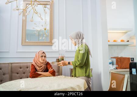 Eine Asiatin im Hijab serviert Snacks, wenn ein Freund aufgebracht wird Stockfoto