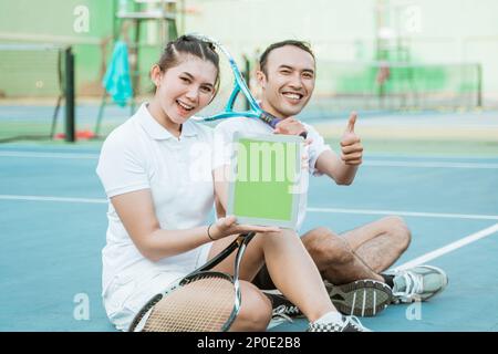 Doppelter Tennisspieler, der sitzt und den Bildschirm des ipads der Kamera zeigt Stockfoto