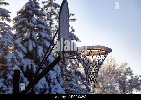 Dieses Bild zeigt eine Nahaufnahme eines schmuddeligen, alten Basketballkörpers und Bändchenbretts, der Schnee von einem kürzlich aufgetretenen Schneesturm enthält Stockfoto