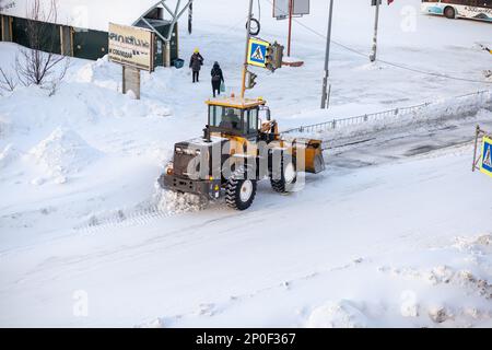 23.01.2023, Kemerovo, Russland. Der orangefarbene Traktor reinigt Schnee von der Straße und lädt ihn in den Lkw. Reinigung und Reinigung von Straßen in der Stadt ab Stockfoto