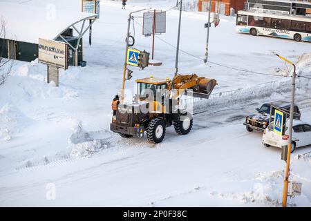 23.01.2023, Kemerovo, Russland. Der orangefarbene Traktor reinigt Schnee von der Straße und lädt ihn in den Lkw. Reinigung und Reinigung von Straßen in der Stadt ab Stockfoto
