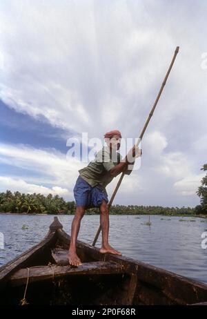 Ein Bootsmann mit einem Puntpfahl auf einem Boot in den Nebengewässern von Kerala, Indien Stockfoto