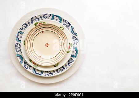 Stapel leer keramische Platten isoliert auf weißem Hintergrund mit Textfreiraum. Fröhlich bunte Gerichte mit Blumenmuster verziert. Schöne vintage Stockfoto