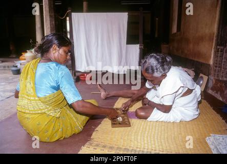 Zwei Frauen, die auf dem Boden saßen und Pallanguzhi spielten in Chettinad, Tamil Nadu, Indien. Pallanguzhi wurde hauptsächlich von Tamilinnen als Zeitvertreib gespielt. Stockfoto