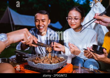 Der Typ im Karohemd lächelt, während er das gegrillte Rindfleisch nimmt Stockfoto