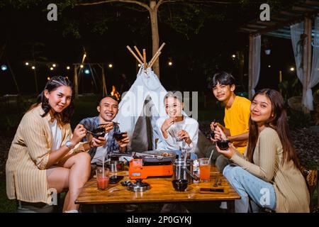 Eine Gruppe von Menschen, die lächeln und das gegrillte Rindfleisch zusammen essen Stockfoto