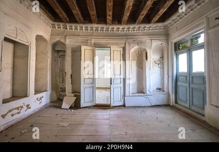 Blick auf ein verlassenes Bauwerk, das jetzt größtenteils ruiniert ist und auf die Restaurierung wartet. Ein schlichtes, weiß getünchtes Nebenzimmer. In einem alten, historischen, klassischen, traditionellen Stockfoto