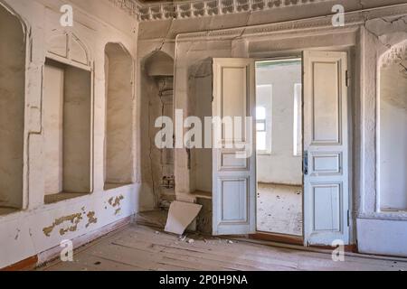 Blick auf ein verlassenes Bauwerk, das jetzt größtenteils ruiniert ist und auf die Restaurierung wartet. Ein schlichtes, weiß getünchtes Nebenzimmer. In einem alten, historischen, klassischen, traditionellen Stockfoto